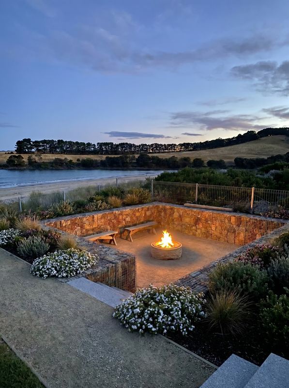 Sunken gabion fire pit with timber benches and native planting on the same estuary site, after
