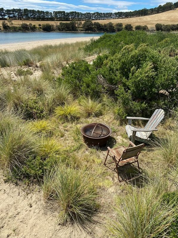 Weathered fire bowl and old chairs on an unplanted dune above the estuary beach, before work